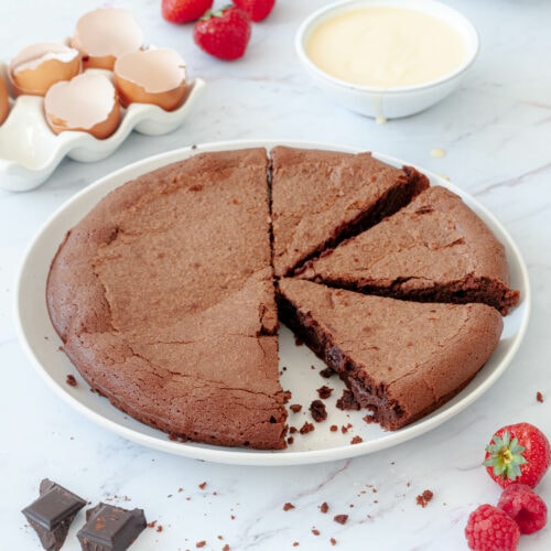 Gâteau dans une assiette entourée de fraises, carrés de chocolat et crème anglaise dans un bol.