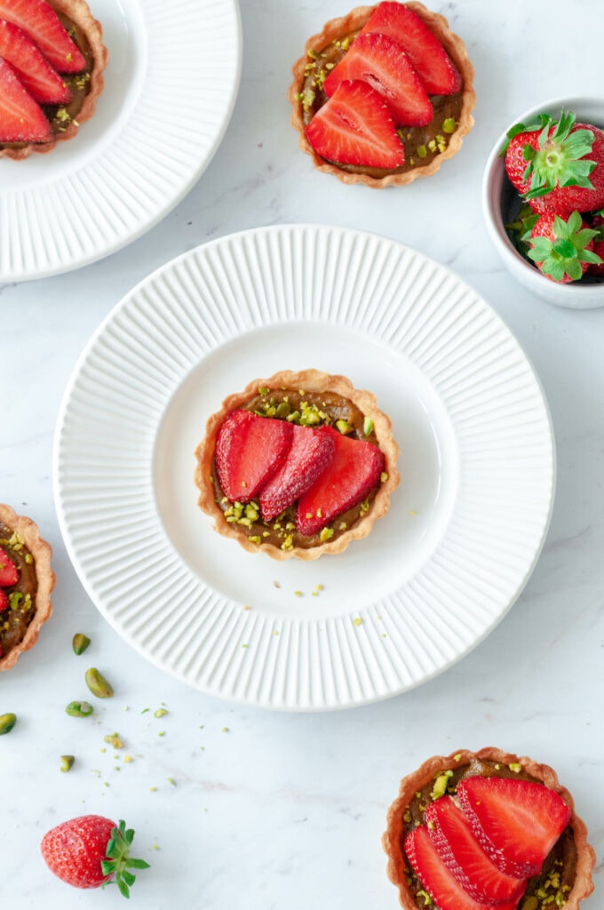 Several tartlets on plates with a bowl of strawberries.