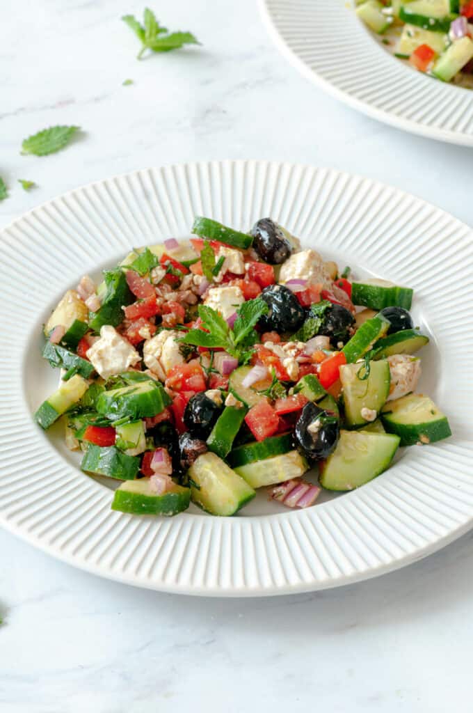 Salade grecque dans une assiette avec quelques feuilles de menthe autour.