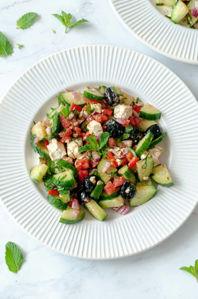 Greek salad on a plate with a few mint leaves around it.