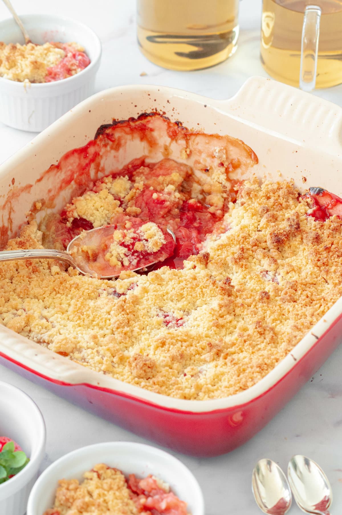 Strawberry and rhubarb crumble in a dish with tea and strawberries in a bowl.