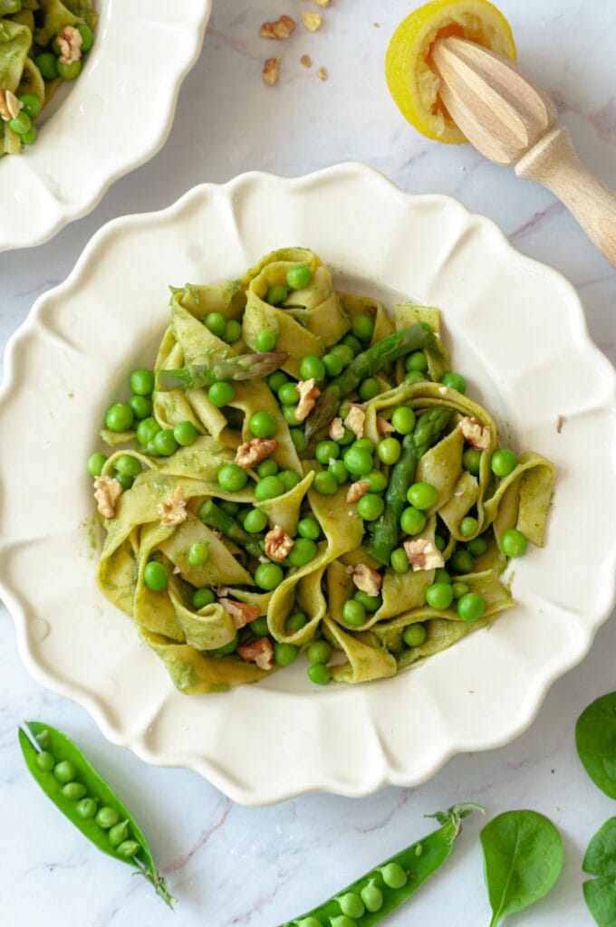 Creamy pasta on a plate with pea pods, a manual lemon squeezer and spinach leaves.