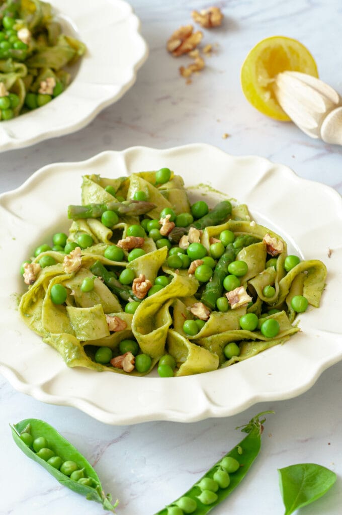 Creamy pasta on a plate with pea pods, a manual lemon squeezer and spinach leaves.