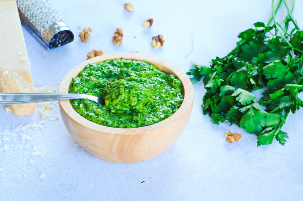 Pesto in a bowl with parsley leaves, a piece of Parmesan cheese and a grater.