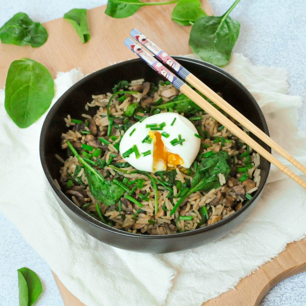 Riz au soja dans un bol avec des baguettes, un oeuf coulant et des feuilles d'épinard.
