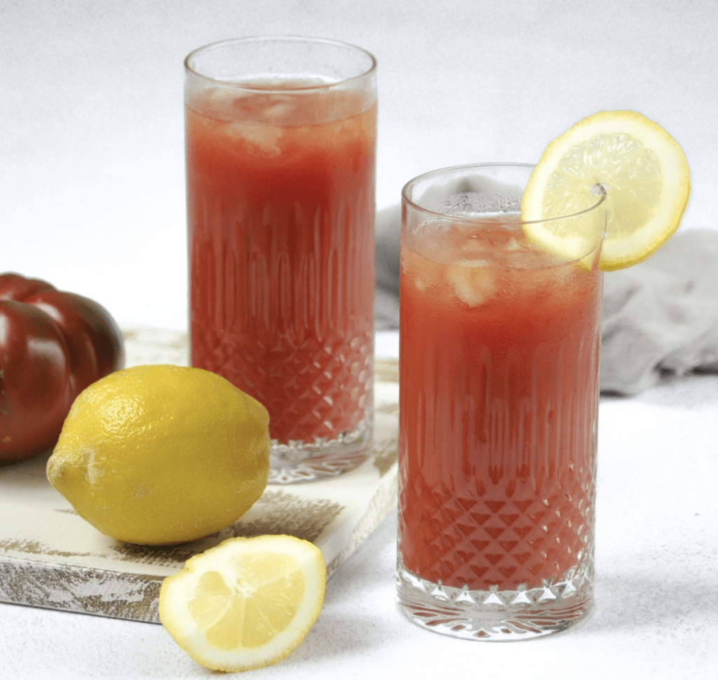 Two glasses of bloody mary with lemon slices and a tomato.