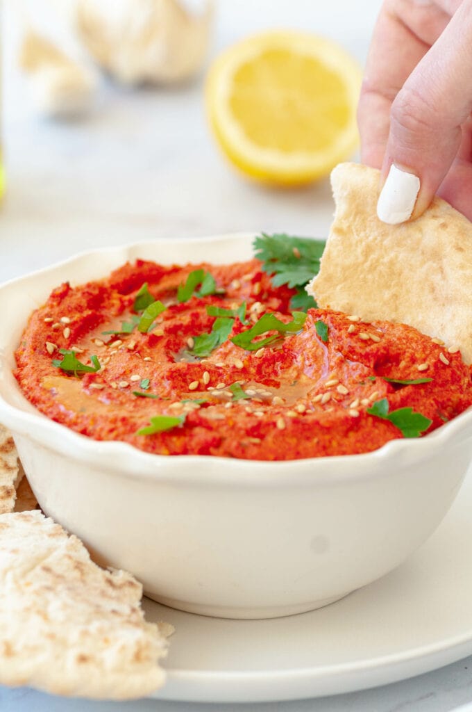 Hand holding a pita and dipping it in Muhammara