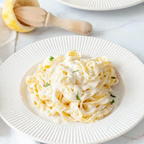 Deux assiettes de Linguine en sauce avec une serviette, un presse-citron en bois et deux demi citrons.