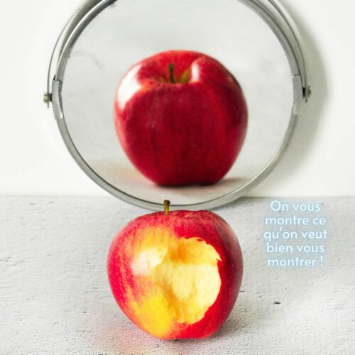 Pomme à moitié croquée devant un miroir qui la montre belle et rouge.