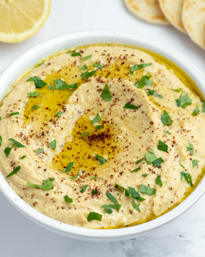 Houmous dans un bol blanc avec un filet d'huile d'olive, du Zaatar et de la coriandre.