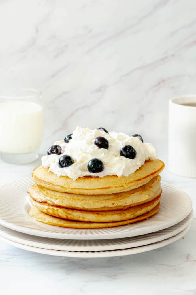 Pile in pancakes on a plate with whipped cream and glass of milk