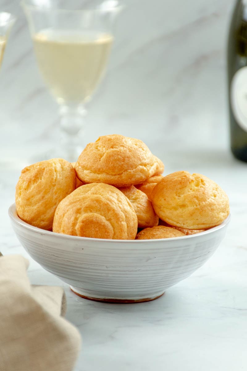 Cheese gougères in a bowl with two glasses of wine.