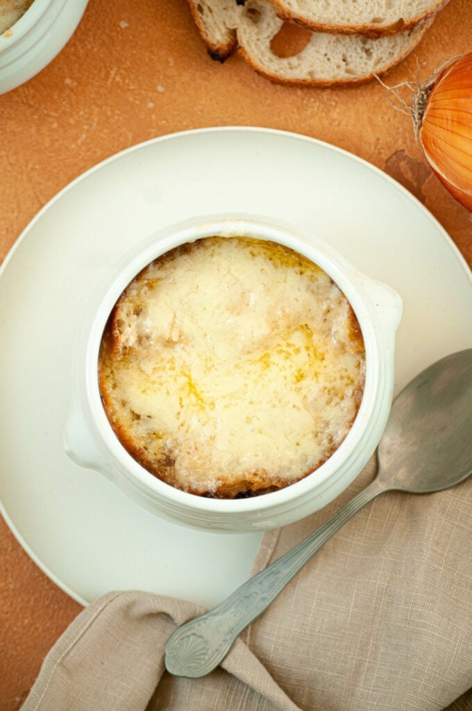 Onion soup in a bowl on a plate with a spoon and napkin.