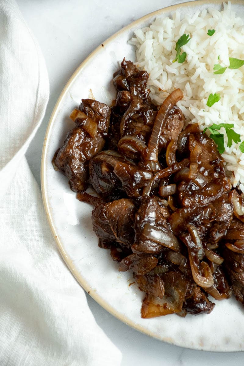 Beef with onions on a plate with rice.