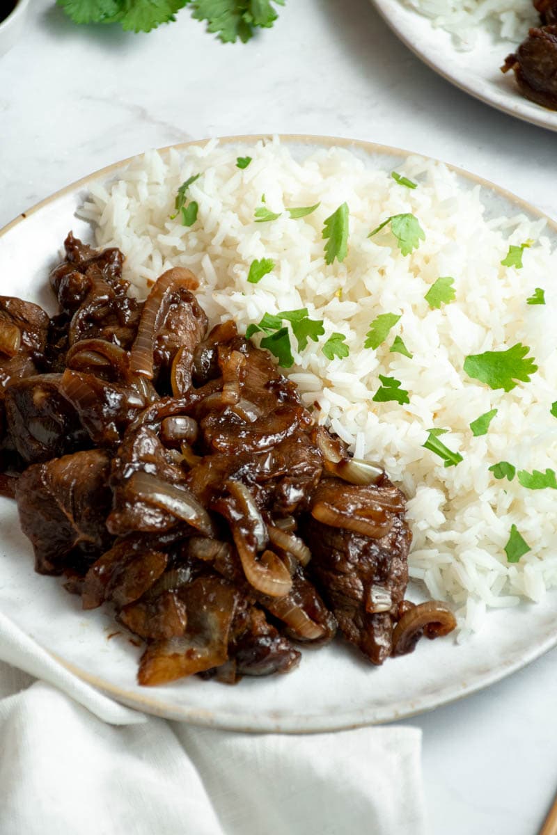 Beef with onions on a plate with rice.