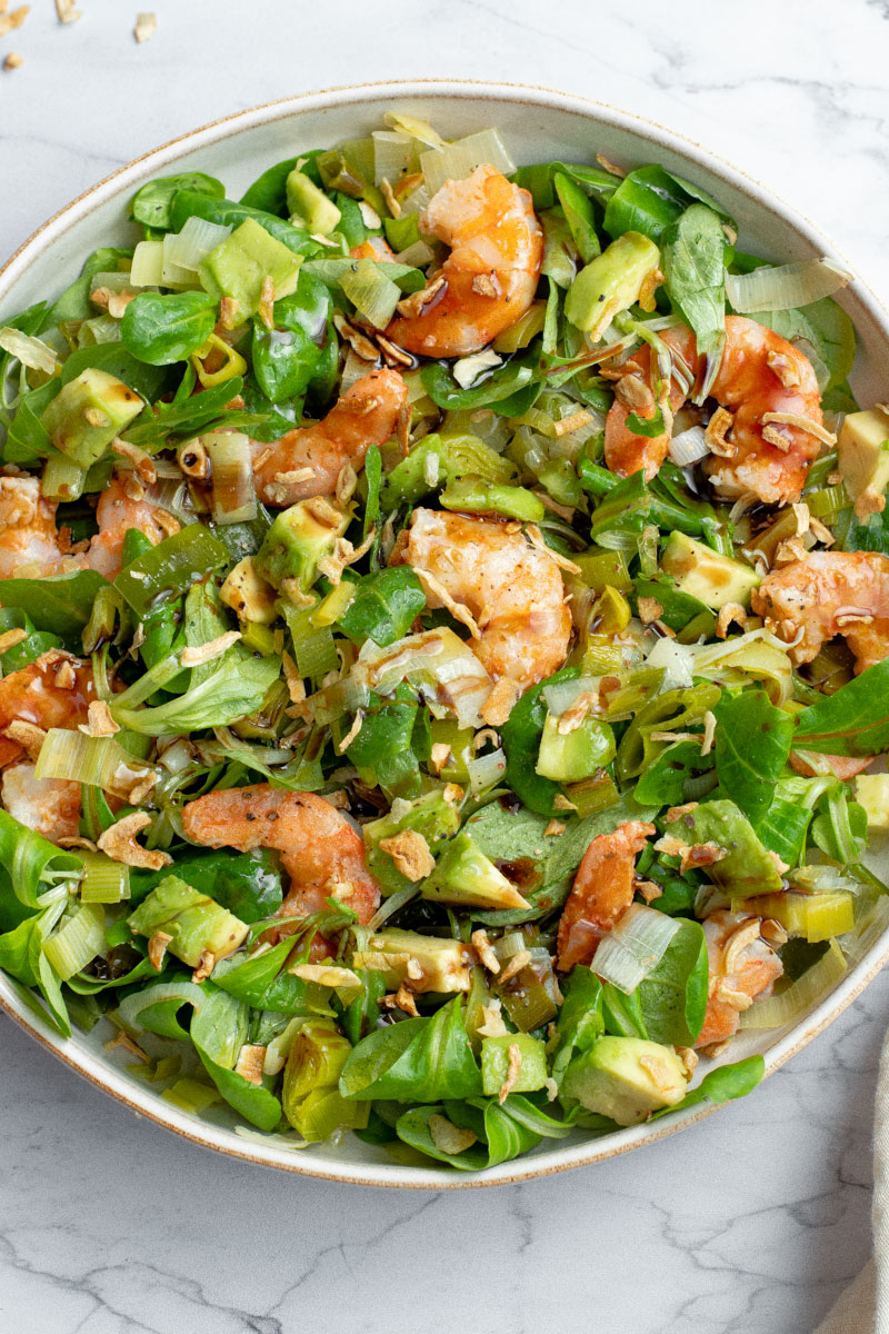 Leek, avocado and shrimp salad in a beige and white bowl.