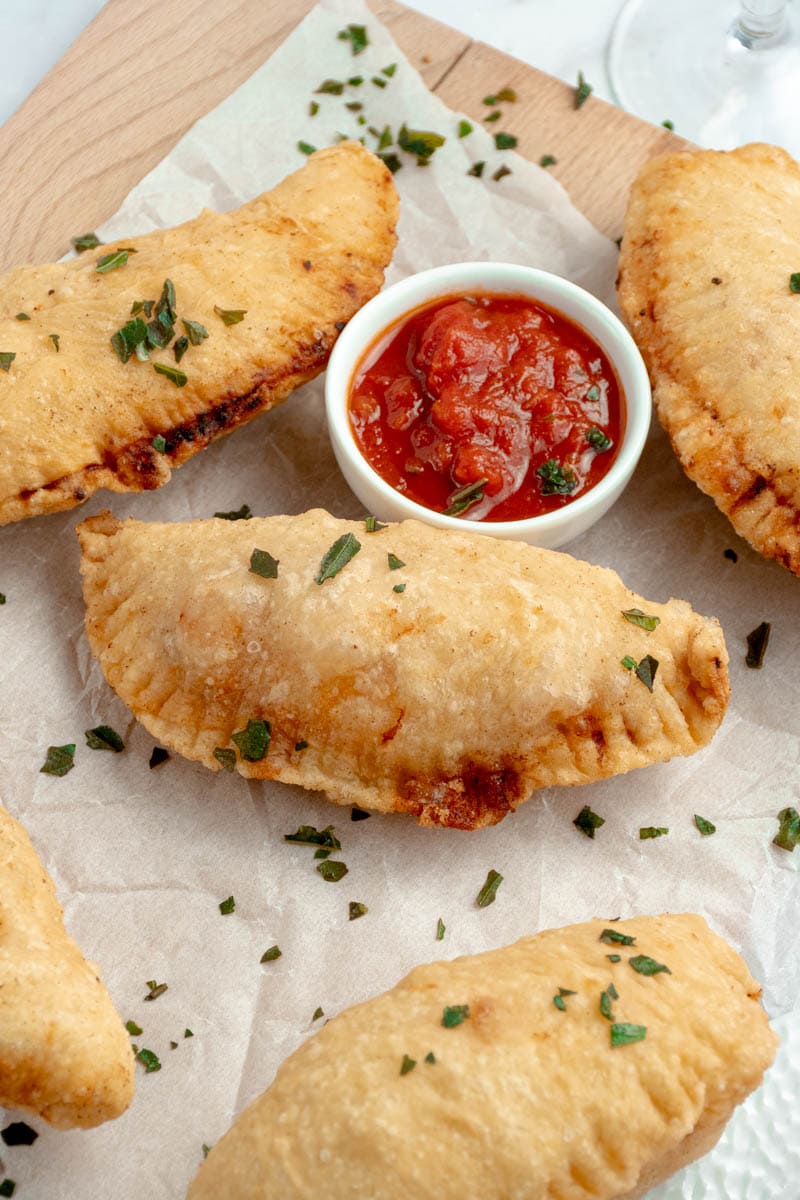 Panzerotti on baking paper with a bowl of tomato sauce.
