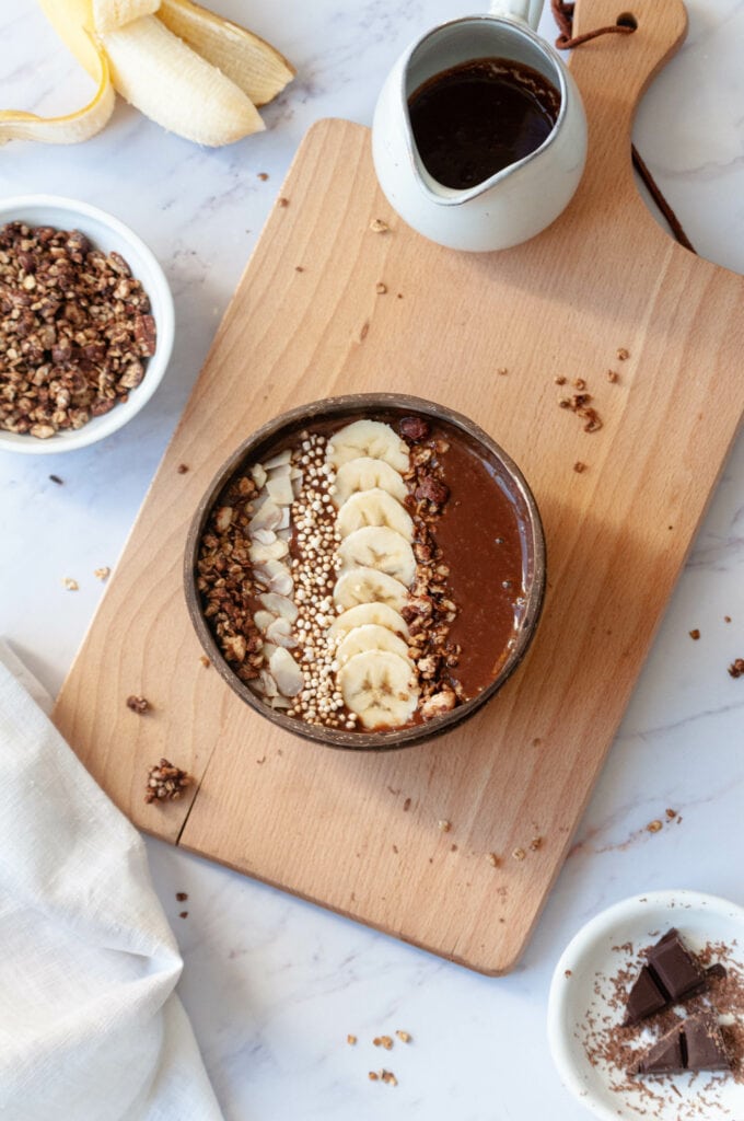 Smoothie bowl, granola in a bowl, pitcher of melted chocolate and a banana.