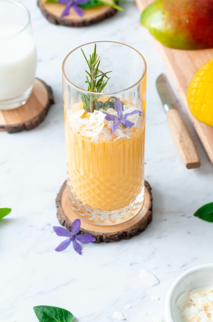 Lassi in a glass with a chopped mango, a glass of almond milk and slivered almonds in a bowl.