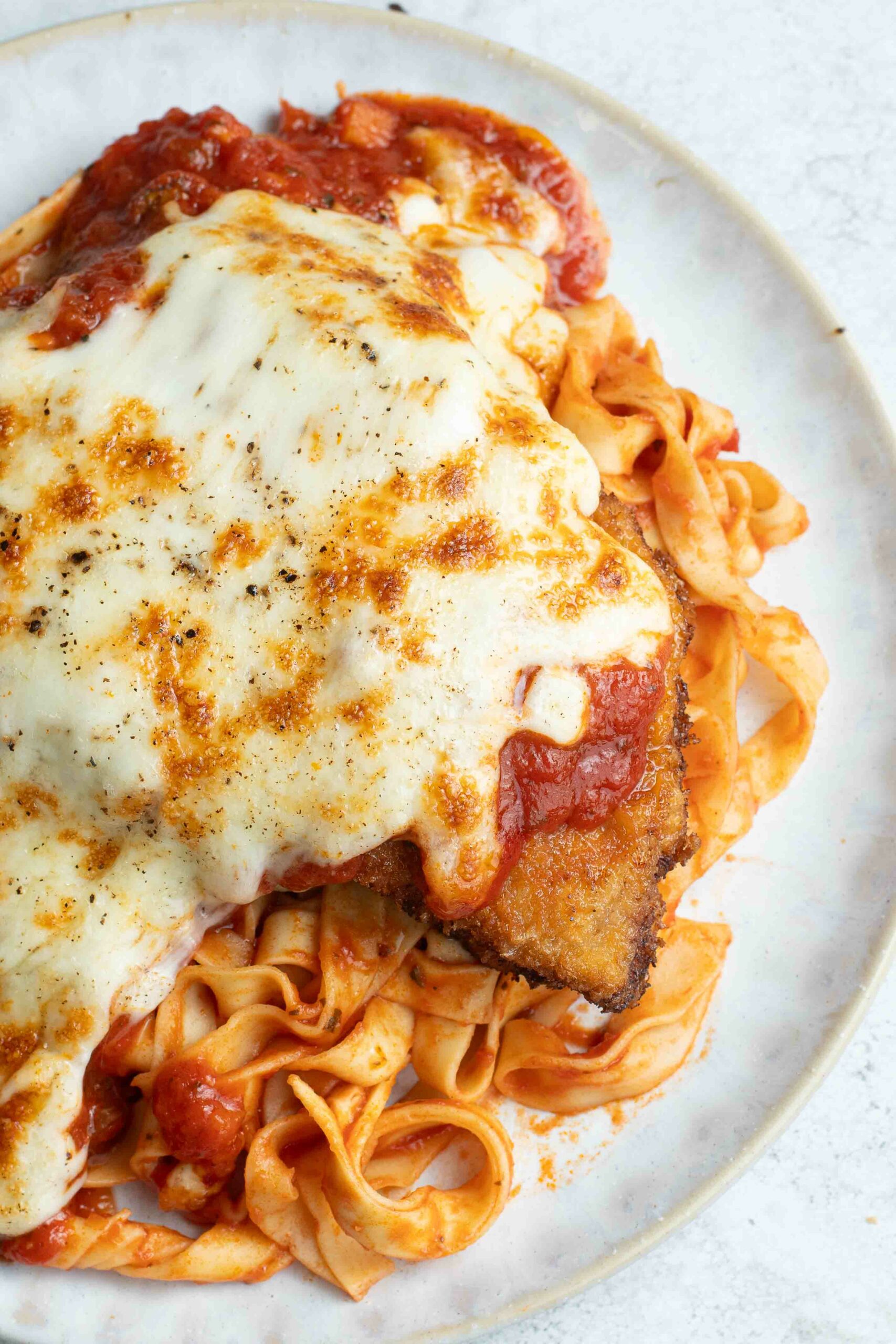 Milanaise à la Napolitaine dans une assiette blanche avec des pâtes à la sauce tomate.