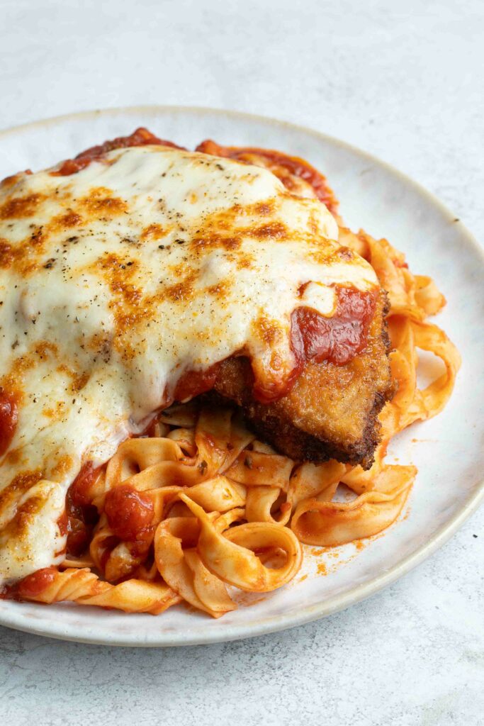 Milanaise à la Napolitaine dans une assiette blanche avec des pâtes à la sauce tomate.