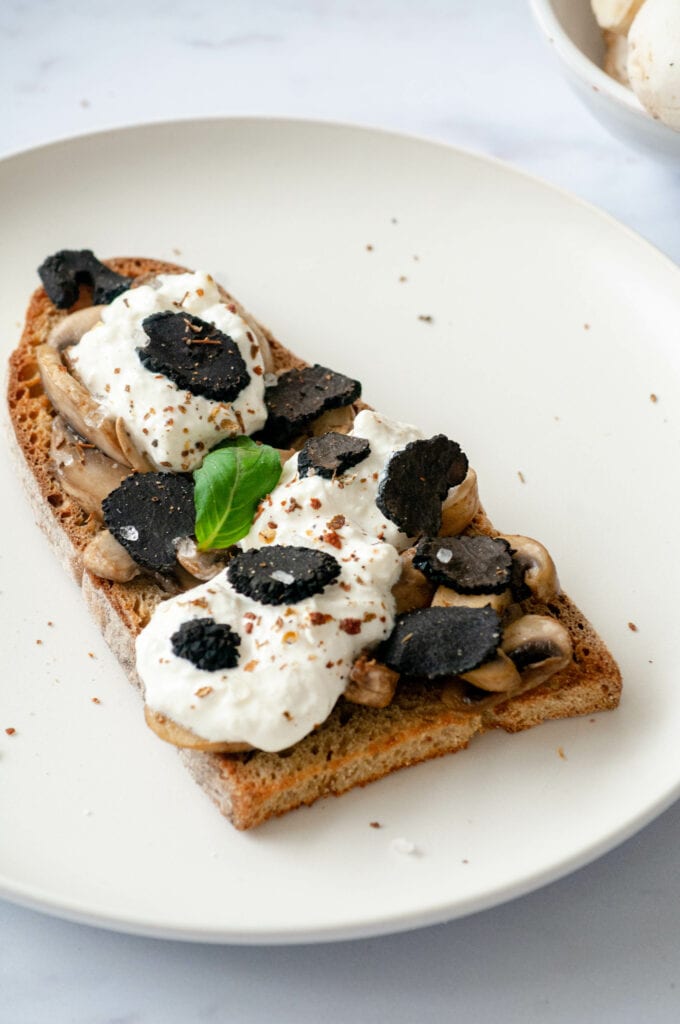 Toast with black truffle, mushrooms and straciatella on a plate.