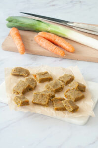 Cubes de bouillon sur du papier cuisson avec des poireaux et des carottes sur une planche.