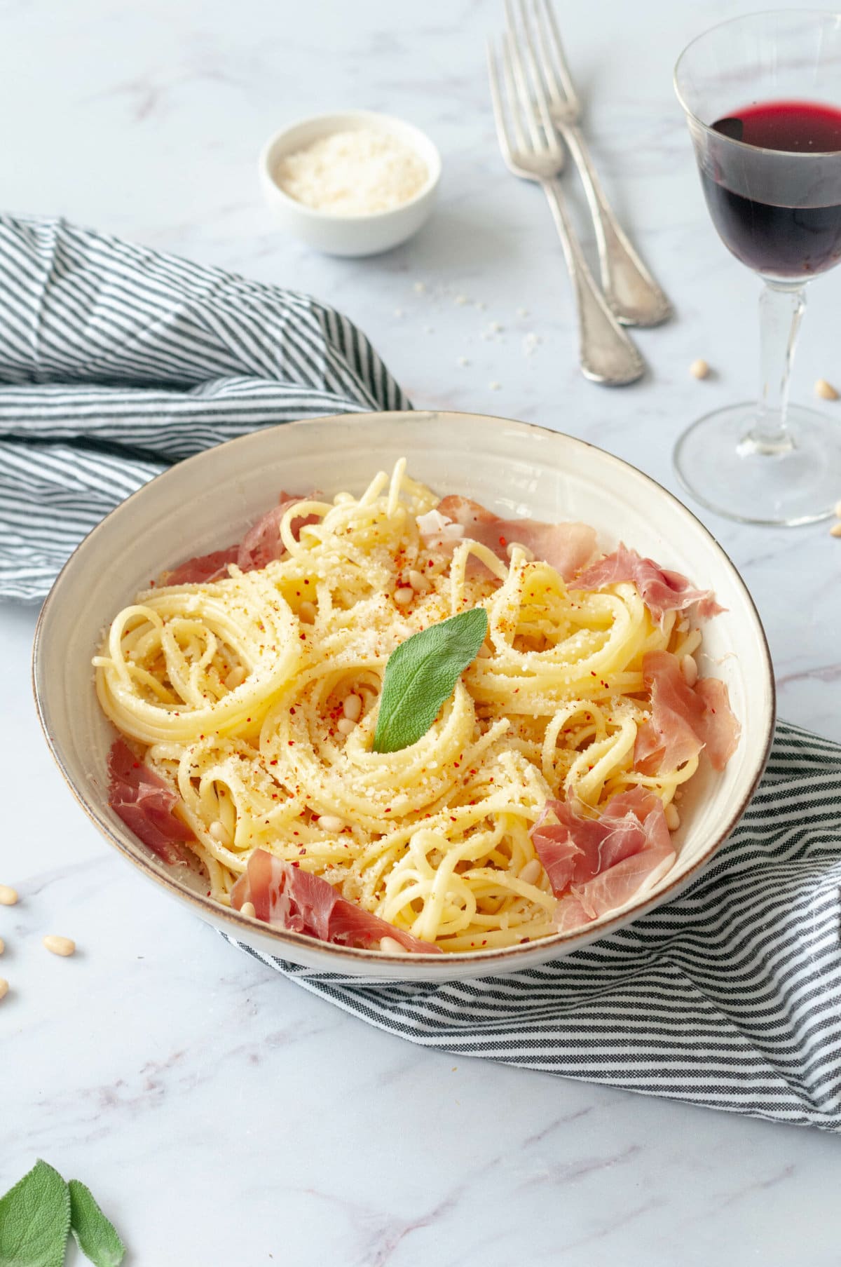 Pasta with sage butter in a bowl with a napkin, a glass of wine and Parmesan cheese.