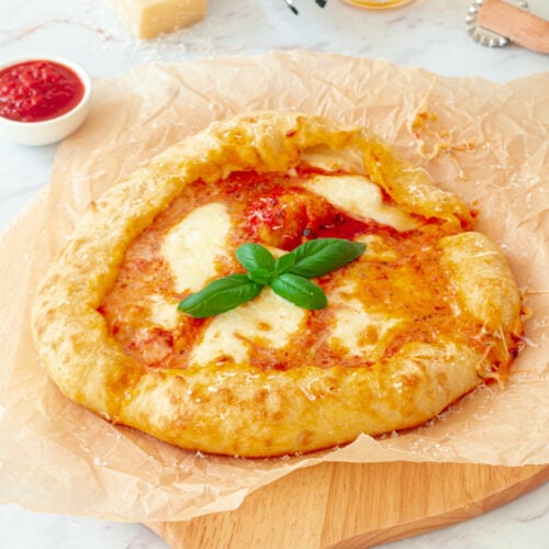 Pizza Margherita sur une planche avec un morceau de Parmesan, un bol de sauce tomate et un verre de bière.