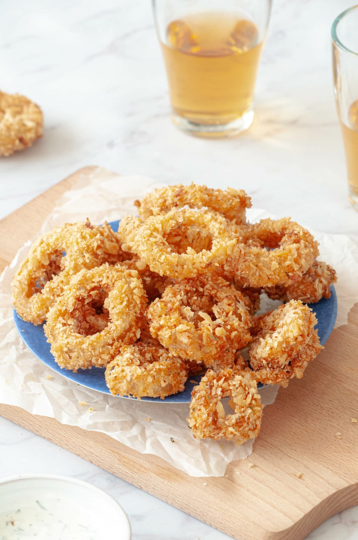 Onion rings on a blue plate placed on parchment paper with two glasses of beer.