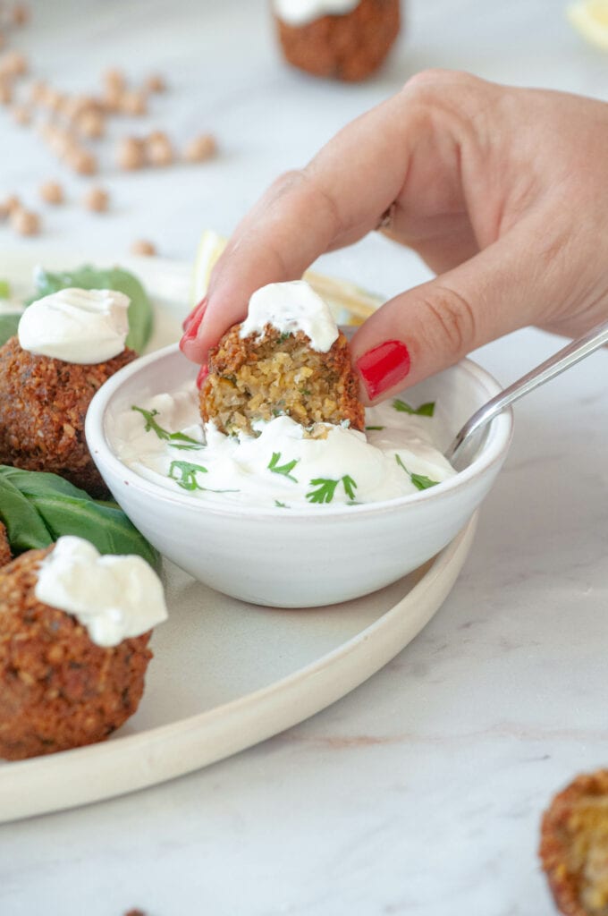 Hand holding a falafel and dipping it in a yogurt and mint sauce.