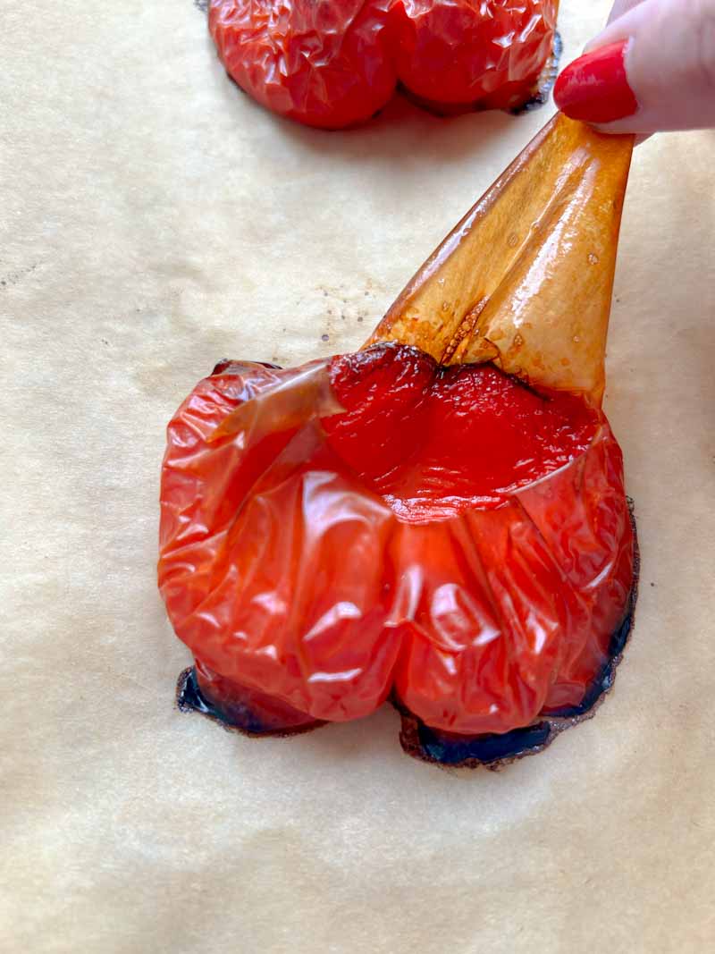 Hand removing the skin from a red bell pepper.