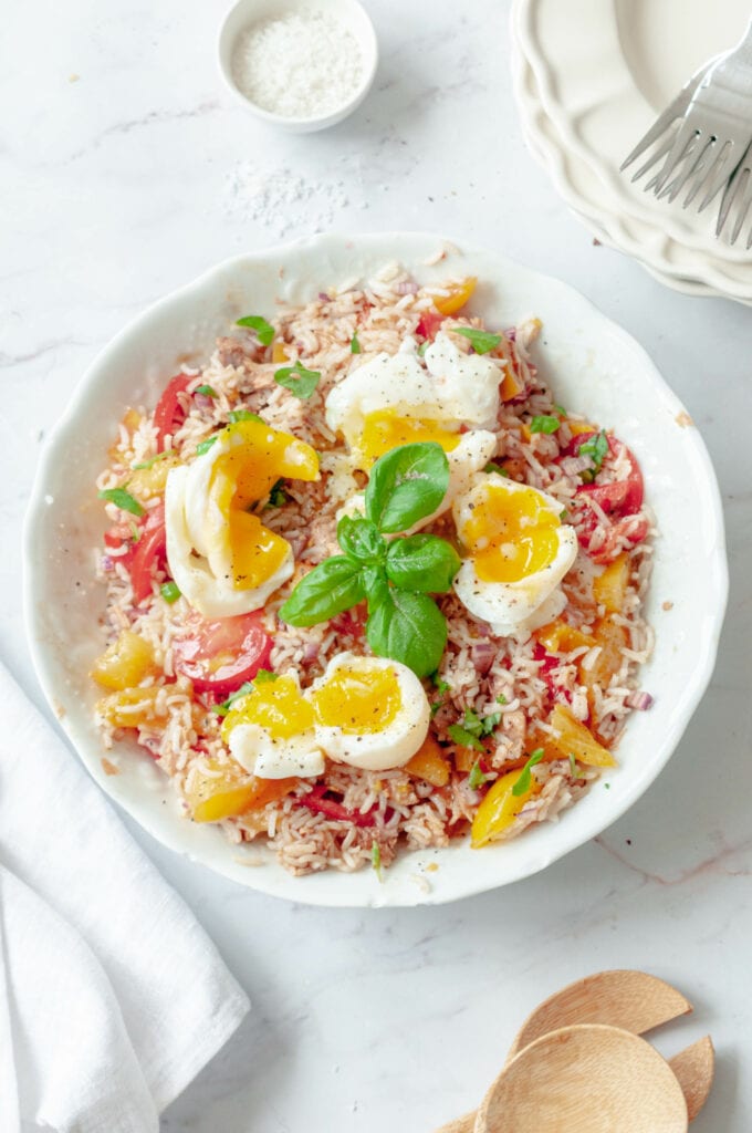 Salade de riz, thon, tomates et oeufs mollets dans un saladier avec des cuillères à salade et un bol de sel.