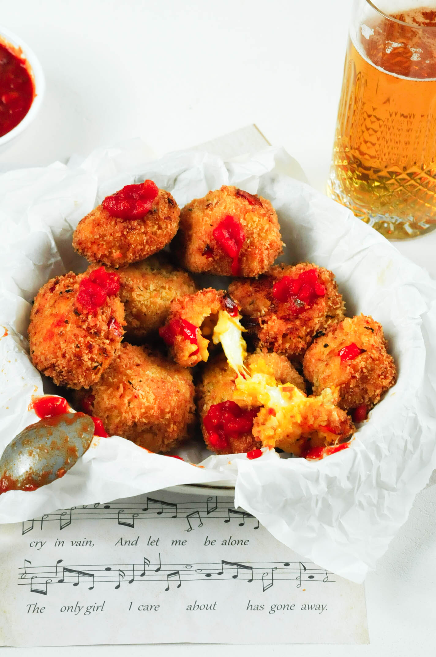 Arancini in a bowl with a spoonful of tomato sauce and a beer