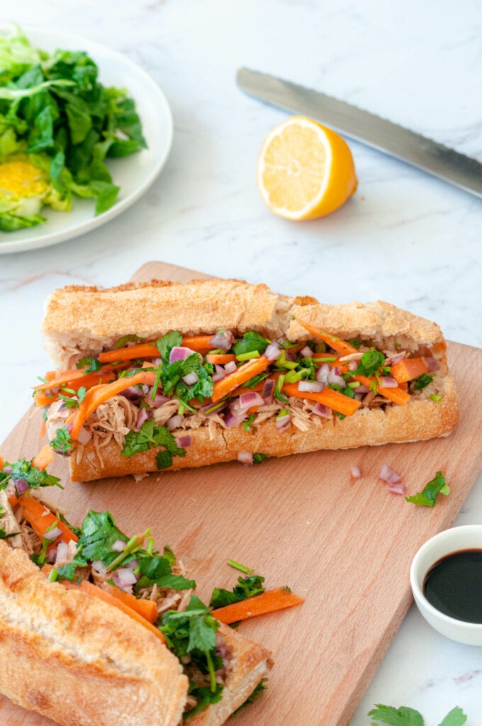Two Banh Mi on a board with a salad and half a lemon.