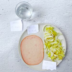 Verre d'eau et assiette avec une tranche de jambon et une sucrine. À côté, les étiquettes avec le nombre de calories.