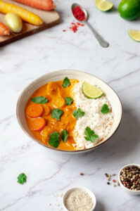 Curry dans une assiette, légumes sur une planche et cuillère de paprika renversée.
