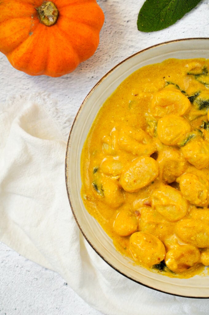 Gnocchi in a bowl with mini pumpkins and a bowl of sage.