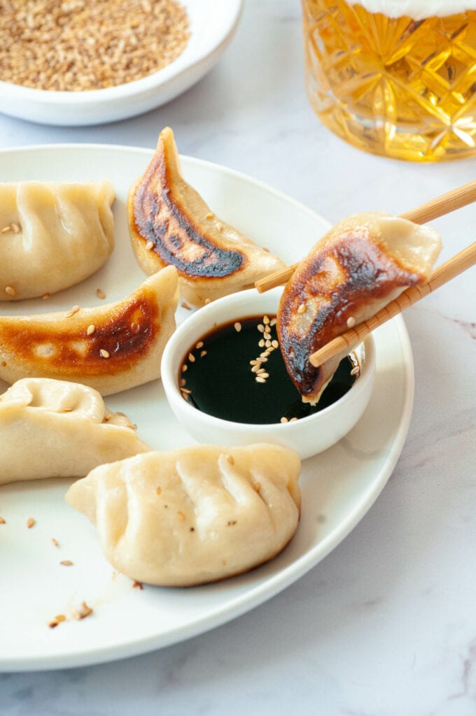 Gyoza tenu par des baguettes et trempé dans la sauce, avec d'autres gyozas autour.