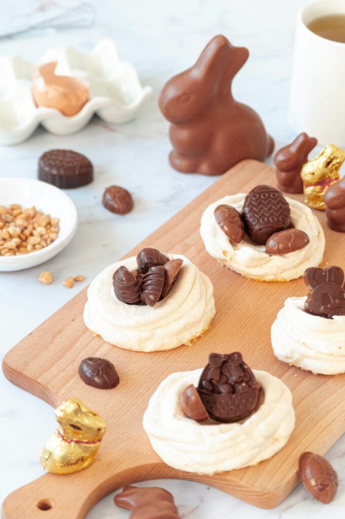 Chocolats pralinés dans leurs nids de meringue sur une planche avec des chocolats autour.