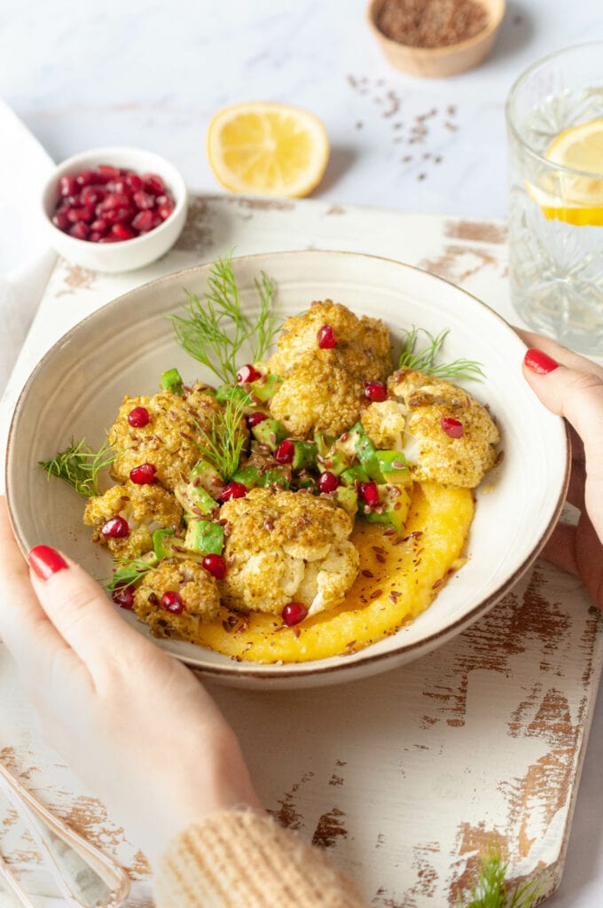 Bowl of polenta, cauliflower and avocado held by two hands on a board.