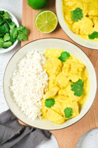 Chicken with coconut milk and curry in two bowls on a board with cilantro and lime.