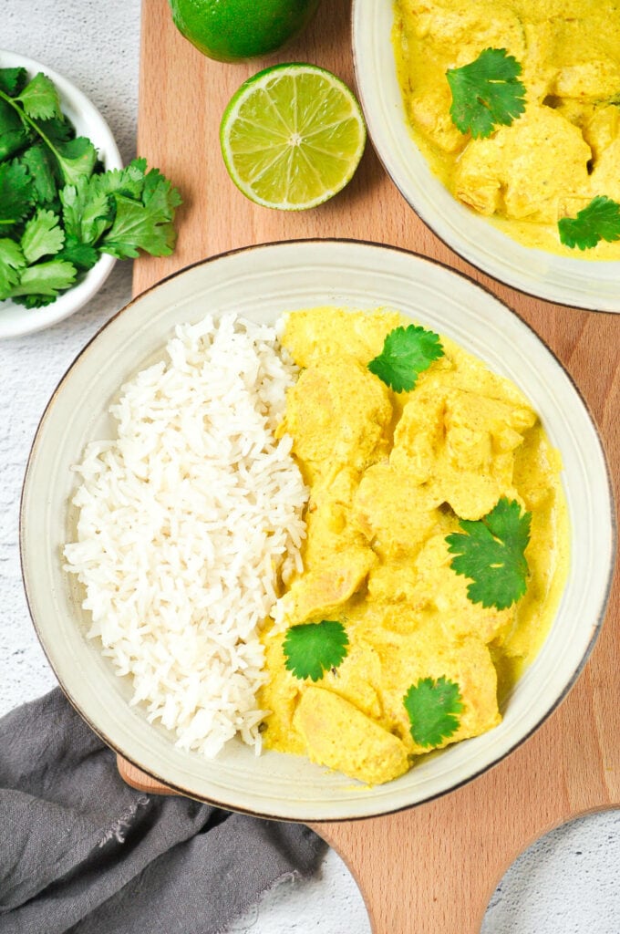 Poulet au lait de coco et curry dans deux bols sur une planche avec de la coriandre et du citron vert.