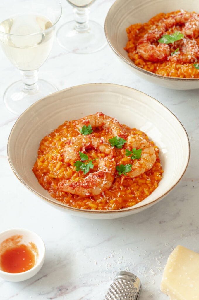 Tomato and scampi risotto in two bowls with glasses of white wine and a jar of tomato sauce.
