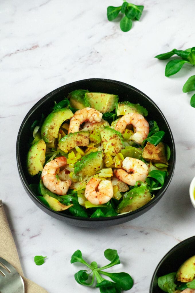 Leek, avocado and shrimp salad in two bowls with lamb's lettuce leaves, napkin and fork