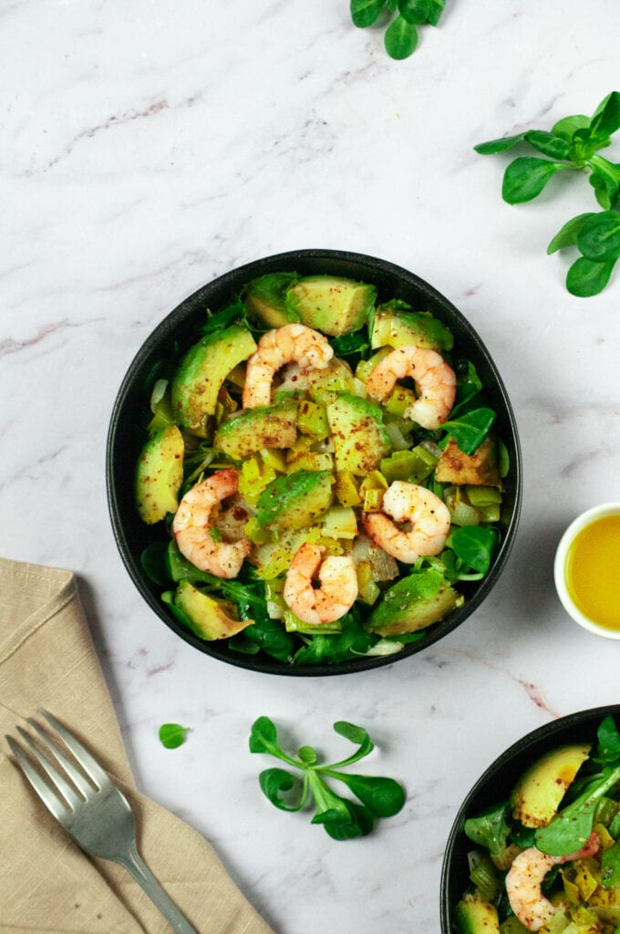 Leek, avocado and shrimp salad in two bowls with lamb's lettuce leaves, napkin and fork