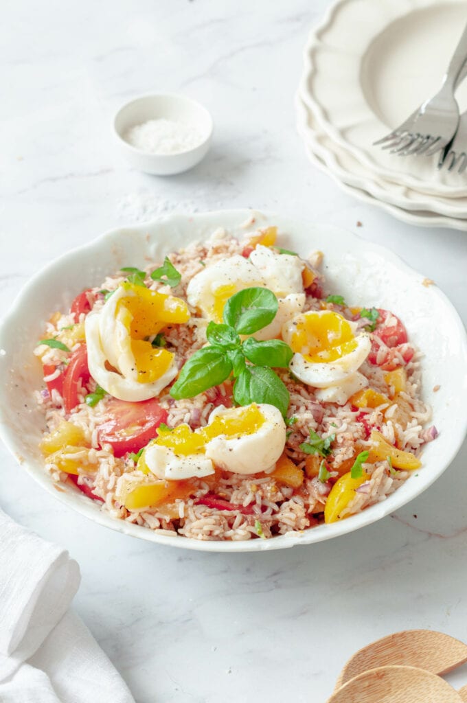Salade de riz dans une saladier avec un petit bol de gros sel ainsi que plusieurs assiettes empilées et fourchettes.