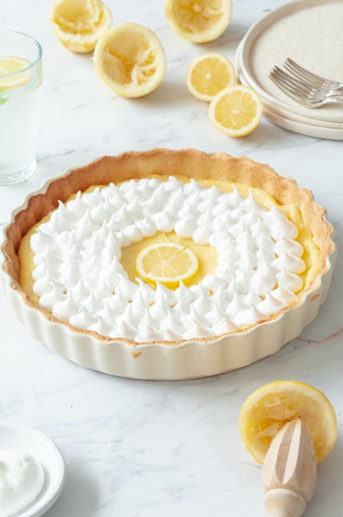 Zoom sur la tarte au citron, avec une meringue, des citrons, des petites assiettes et une eau citronnée.