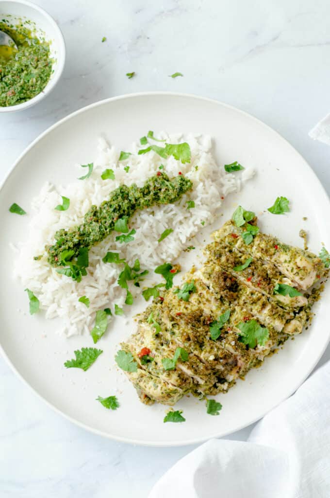 Escalope de poulet émincée dans une assiette blanche avec du riz, la sauce chimichurri et quelques feuilles de coriandre.