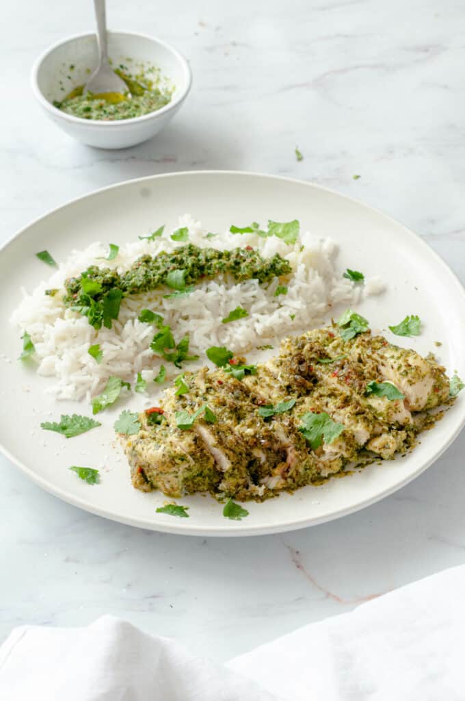 Sliced chicken cutlet on a white plate with rice, chimichurri sauce and a few coriander leaves.